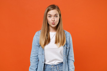 Fototapeta premium Pretty young woman girl in casual denim clothes posing isolated on bright orange wall background studio portrait. People sincere emotions lifestyle concept. Mock up copy space. Blowing cheeks, lips.