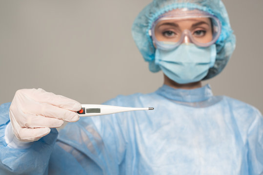 Selective Focus Of Doctor In Safety Googles Holding Thermometer Isolated On Grey