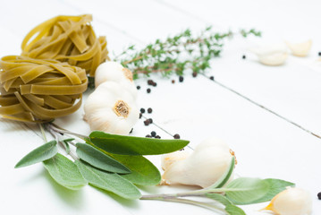 raw tagliatelle pasta, garlic and spice leaves on white wood table background