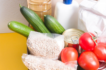 box with products for donation, yellow background, copy space, cereals, vegetables, fruits, oil in a bottle, flour and canned food in a box, hygiene product and protection against coronavirus.