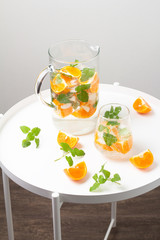 glass and carafe with a drink with orange and mint on a white table close-up
