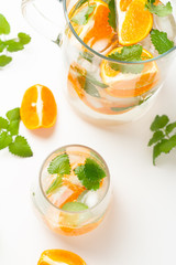 carafe and glass with a drink with orange mint and ice on the table

