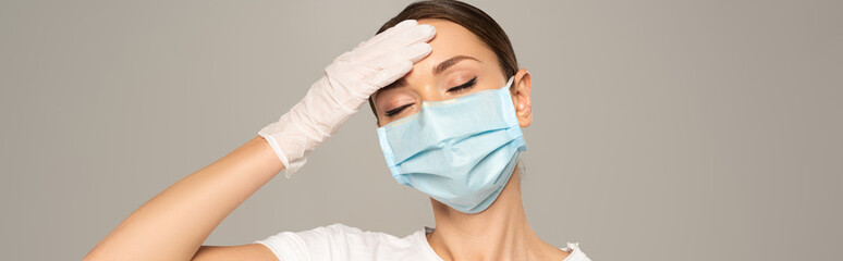 Fototapeta premium Panoramic shot of woman in medical mask touching forehead isolated on grey
