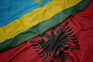 waving colorful flag of albania and national flag of rwanda.
