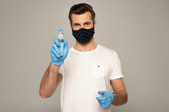 Man In Latex Gloves And Safety Mask Holding Hand Sanitizer Isolated On Grey