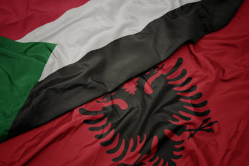 waving colorful flag of albania and national flag of sudan.