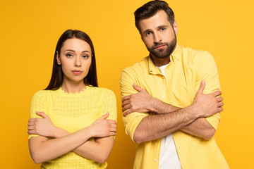 Young couple with crossed arms looking at camera on yellow background
