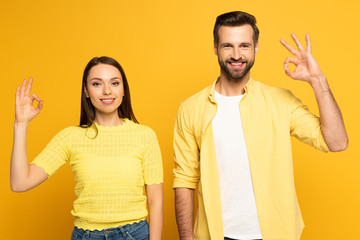 Smiling young couple showing okay gesture on yellow background