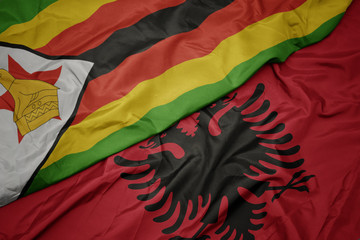 waving colorful flag of albania and national flag of zimbabwe.