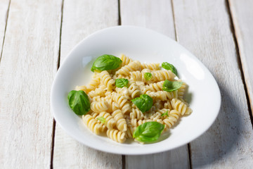 fusilli pasta with basil leaves and cheese  on white wooden background