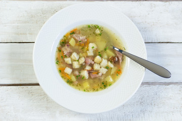 Pea soup with smoked meat and potato, toast, spoon in white plate on rustic background