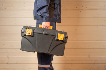 Concept of construction and repair, image of a toolbox in the hands of a builder or worker close up against a wooden wall