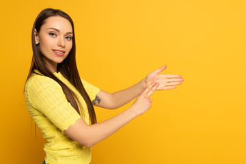 Side view of smiling woman using sign language on yellow background