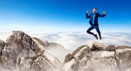 Young businessman feels success and jumps up over mountains