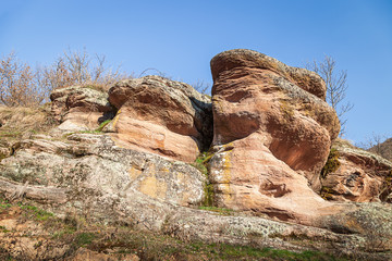 Beautiful shapes of eroded red rocks covered by golden, sunlit moss under a blue sky in a canyon in...