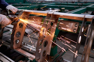 Processing a metal product using a manual grinder. A worker using a grinder cut metal