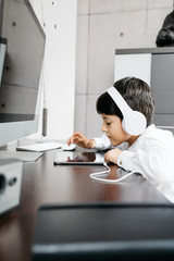 A little boy wearing a white shirt holding for a photo with white headphones