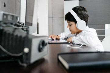 A person standing in front of a computer with white headphones and touching a tablet