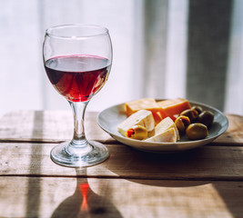 Glass with red wine and a plate with appetizers, with cheese and stuffed olives on a wooden table, retro toning image
