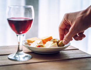 Glass with red wine and a plate with appetizers, with cheese and stuffed olives on a wooden table, retro toning image