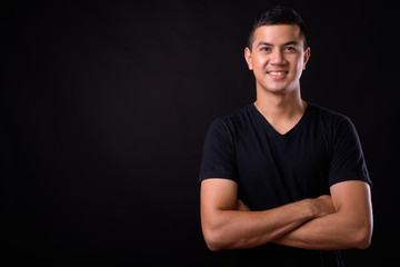 Portrait of happy young handsome Asian man smiling with arms crossed