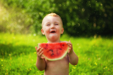 Portrait of little kid without t-shirt in the village, on the fresh air. Two years old
child eating piece of watermelon on the grass in garden. Dirty face, happy and emotional
kid, juicy watermelon.
