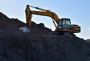 Excavator working at open pit mining. Backhoe digs gravel in sand quarry on blue sky background. Recycling old asphalt at a landfill for the disposal of construction waste