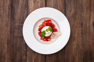 Fresh Burrata cheese with tomatoes  on a plate on a wooden table.