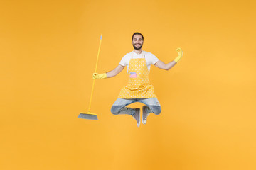 Smiling young man househusband in apron rubber gloves hold broom while doing housework isolated on...