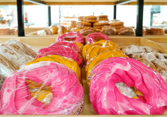 Pink and yellow choux donuts, various baked goods and puff pastry serving for sell on a shelfs in...