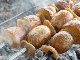 Potato on a skewer. Vegetarian kebab. Potato with bacon cooking on charcoal.