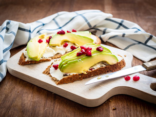 Vollkornbrot mit Avocado und Granatapfelkernen auf einem Schneidebrett und ein kariertes...