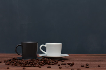 White and grey cup of coffee on brown wooden table with scattered beans on dark blue wall background. Closeup, copy space, side. Coffee shop, cafe, morning, breakfast, drink  concept