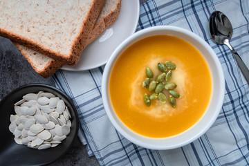 Homemade Pumpkin soup in a bowl with Whole wheat bread and pumpkin seeds, top view, copy space. Seasonal autumn food. vegan food