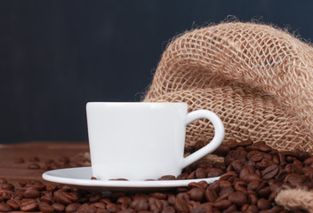 White cup of espresso against blue wall background. Dark roasted coffee beans on burlap jute sack. Closeup, side view. Agriculture, coffee shop, breakfast concept