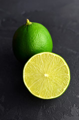 Two green limes on black slate background. The whole one and one cutted.