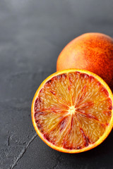 Two red oranges on grey slate background. One whole fruit and one cutted. One whole fruit and one...