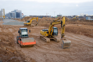 Excavators and soil compactor during road works at construction site. Backhoe digging the ground...