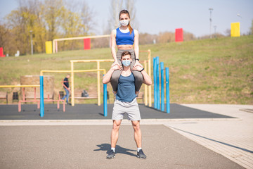 Fototapeta premium Athletic guy and girl doing leg exercises in medical masks during a pandemic. Squats COVID-19. Health care.