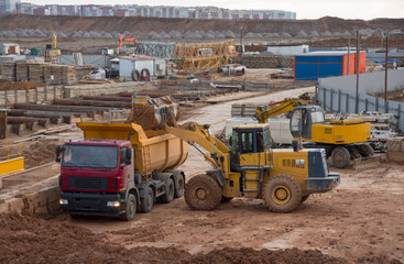 Wheel front-end loader loading sand into dump truck at the construction site