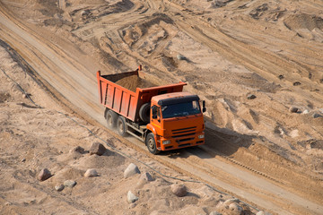 Orange dump truck transports sand in an open pit mine. In the production of reinforced concrete...