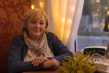 portrait of an elderly woman sitting at the window in a cafe restaurant in the evening on a date