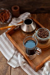 A cup of coffee on a wooden tray. Turk and coffee beans. Cook breakfast at home. Still life with a drink in a glass. Ground coffee, brew and prepare a tonic morning drink.