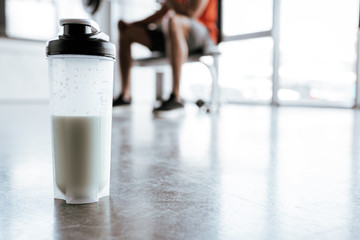 selective focus of sports bottle with protein milkshake near sportsman in gym