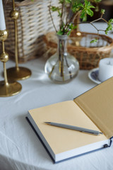 gray pen on a beige book lie on a table on a white tablecloth golden candlesticks greens in a vase wooden basket