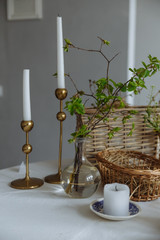 glass transparent vase with greenery golden candlesticks candle and wooden basket on a white background in the interior