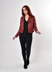 Portrait of a pretty girl with red hair wearing black jeans and boots with leather jacket.  full...