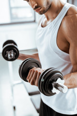 cropped view of athletic sportsman exercising with dumbbells in gym