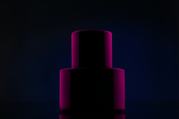 Bottle of black perfume in pink light on a blue background. Cosmetic perfume black