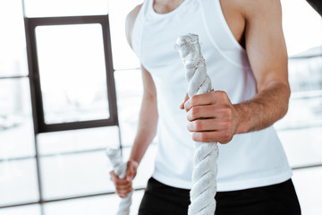 cropped view of sportsman exercising with battle ropes in gym